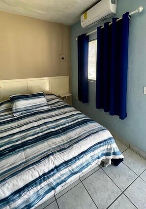 Una habitación con cama, ventana con cortinas y equipo de aire acondicionado.