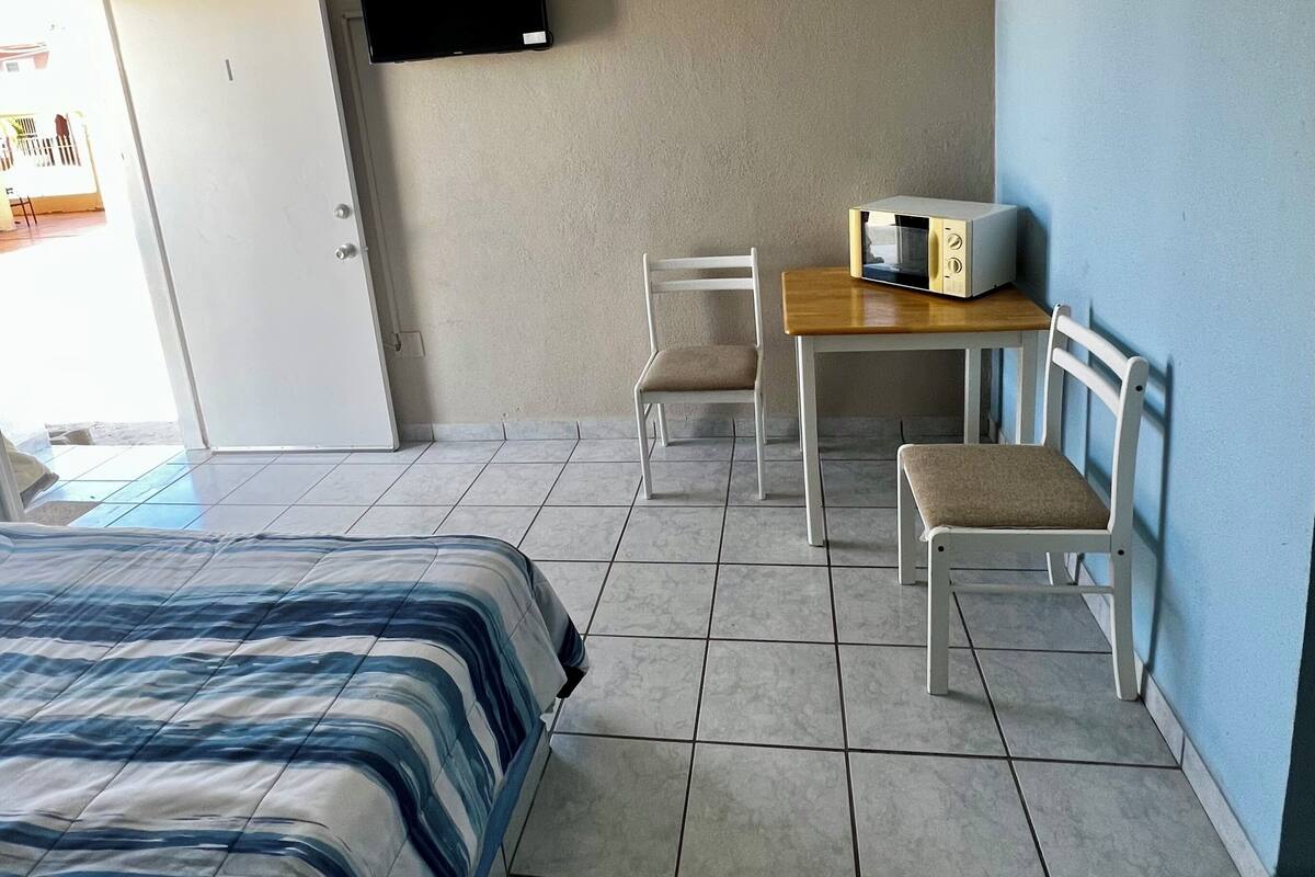 Ein Hotelzimmer mit Bett, Schreibtisch mit eingebauter Mikrowelle, Stuhl und einem an der Wand befestigten Fernseher.