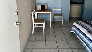 A small, tiled room with a bed, a table, two chairs, a microwave, and a TV mounted on the wall. - Cozy Rooms Rocky Point - Walk to Playa Hermosa (Puerto Penasco)