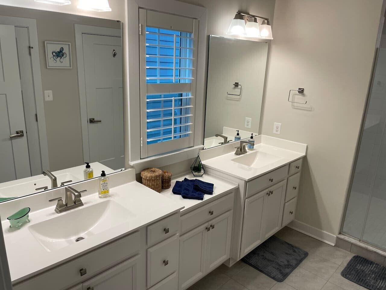 A bathroom with two sinks, a large mirror, and a window with blinds.