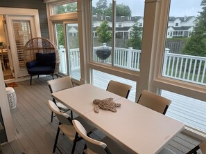 A covered outdoor dining area with a table and chairs, a wicker chair, and a view of a neighborhood. - Dog friendly| community pool | gym| kayak| bayside (Selbyville)