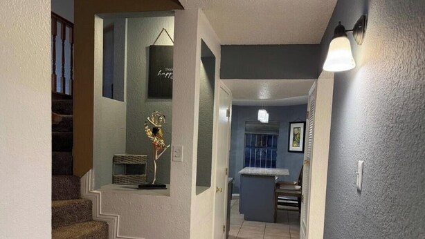Una escalera conduce a una plataforma decorada con una escultura de metal ornamental, una pequeña mesa con una silla y un accesorio de iluminación en la pared.