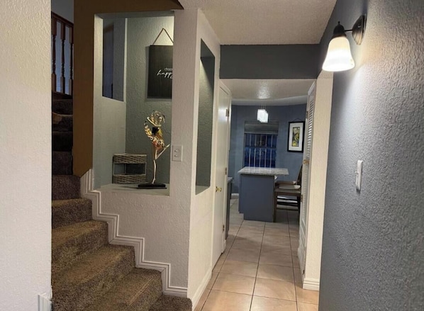A staircase leading to a landing with a decorative metal sculpture, a small table with a chair, and a light fixture on the wall.
