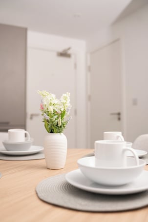A dining table with white ceramic plates and cups, a white vase with flowers, and a wooden table.. Salford apartment near trafford park