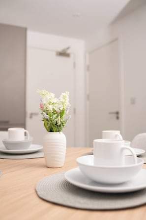 A dining table with white ceramic plates and cups, a white vase with flowers, and a wooden table.
