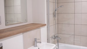 Un baño con lavamanos blanco, un espejo, encimera de madera y zona de ducha con paredes de azulejos.
