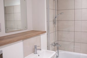 A bathroom with a white sink, a mirror, a wooden countertop, and a shower area with tiled walls.