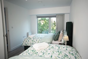A bedroom with two beds, a large window, and a nightstand with a lamp.