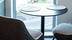 Una habitación con ventana, una mesa redonda con dos individuales y dos sillas.