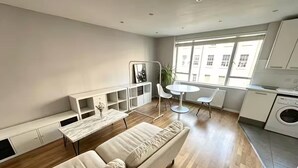 Een modern appartement met een bank, een eettafel, een kleine keuken en een groot raam.