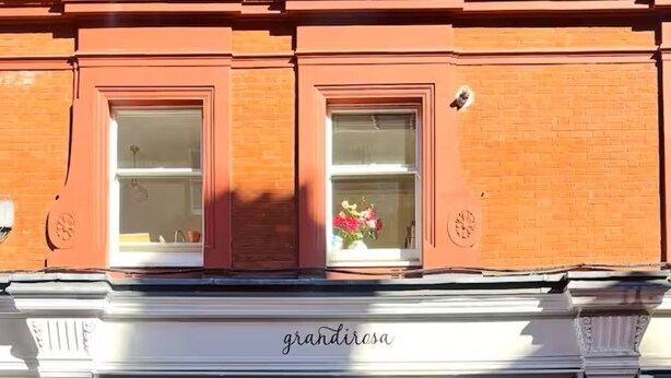 Een etalage met een witte luifel, de naam 'grandirosa' erop en diverse bloemen en planten voor de winkel.