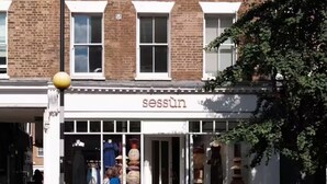 Een winkelgevel met het bord 'sessun' en een voetganger die oversteekt voor de winkel.