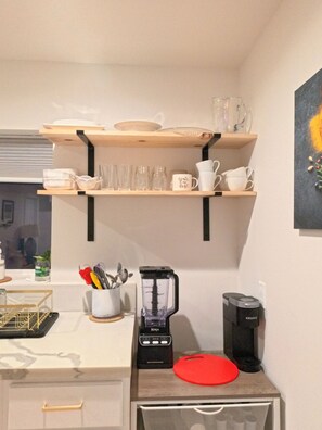 Eine Küche mit Kaffeemaschine, Mixer und Regalen mit Geschirr und Gläsern.