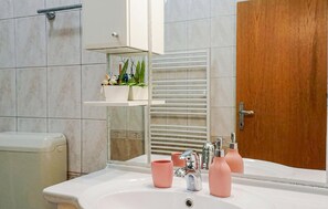 Ein Badezimmer mit weißem Waschbecken, einem Spiegel, einem Handtuchhalter und einer Holztür.