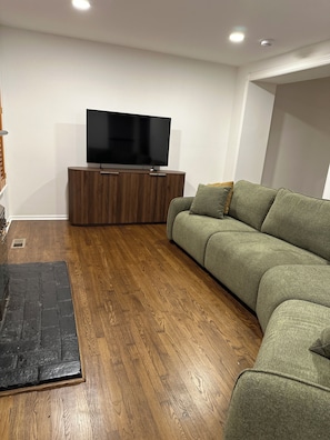 Een moderne woonkamer met een flatscreen televisie op een houten kast, een groene bank en houten vloeren.