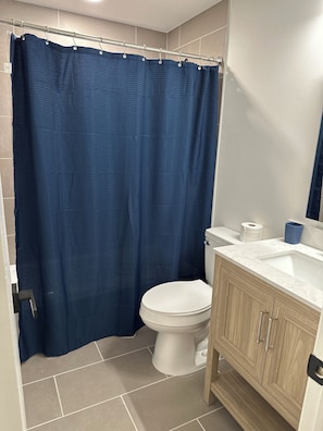 Een badkamer met douchegordijn, toilet, wastafel en houten kastjes.