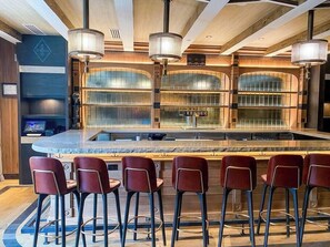 Una zona de bar con mostrador curvo, taburetes y lámparas colgantes.