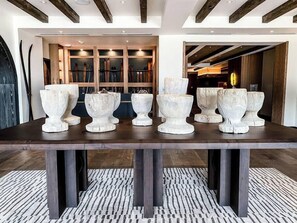 Una mesa de comedor con seis jarrones blancos y ornamentados sobre un suelo de madera oscura.