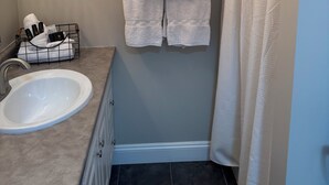 Une salle de bain équipée d’un lavabo, d’un porte-serviettes avec deux serviettes, d’un rideau de douche et d’un autre porte-serviettes avec des articles de toilette.