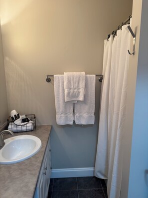 A bathroom with a sink, a towel rack with two towels, a shower curtain, and a towel rack with toiletries.