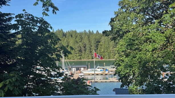 Une terrasse en bois offrant une vue sur une marina, les bateaux amarrés et un drapeau canadien.
