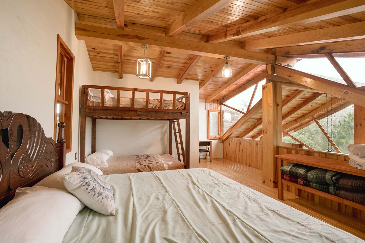 A wooden cabin bedroom with a bunk bed, a desk, and a view through a window.