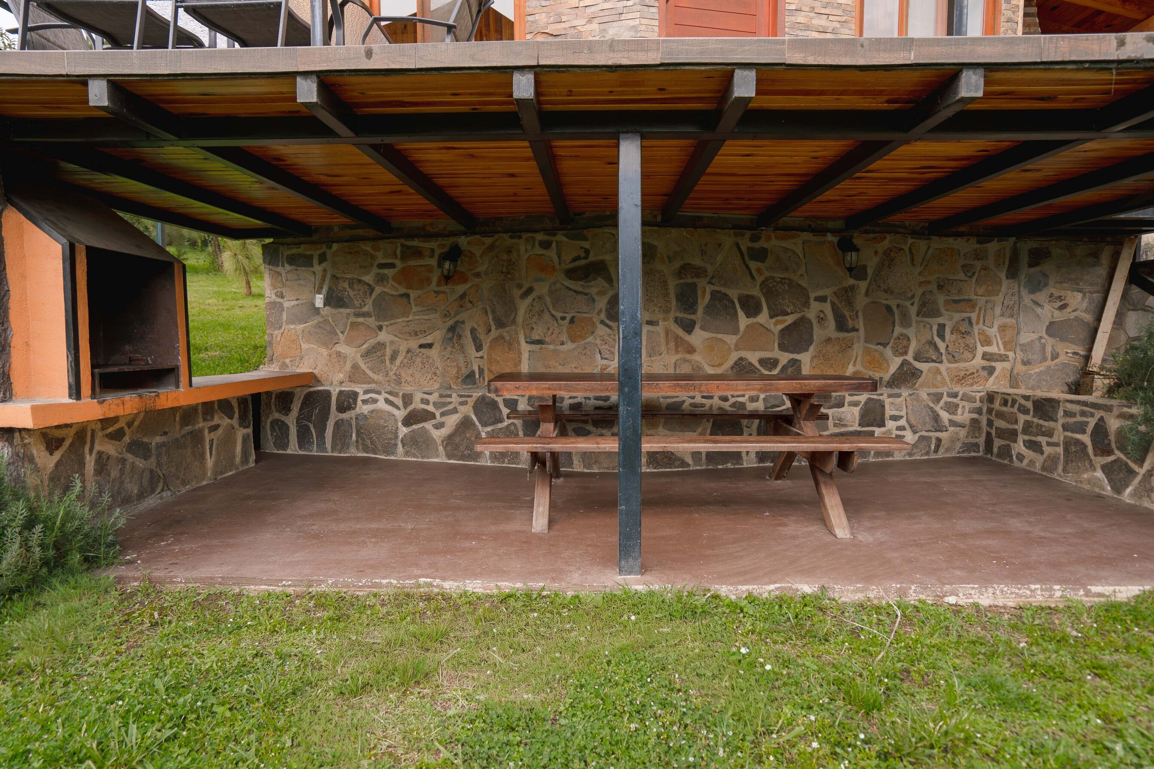 Un patio al aire libre con una pared de piedra, una mesa de madera y un banco.