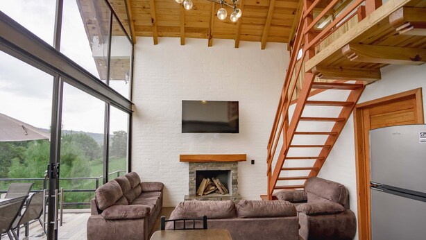 A modern living room with a fireplace, a sofa set, a dining table, and a TV mounted on the wall. - Paseo del Llano Grand Cabañas (Mazamitla)