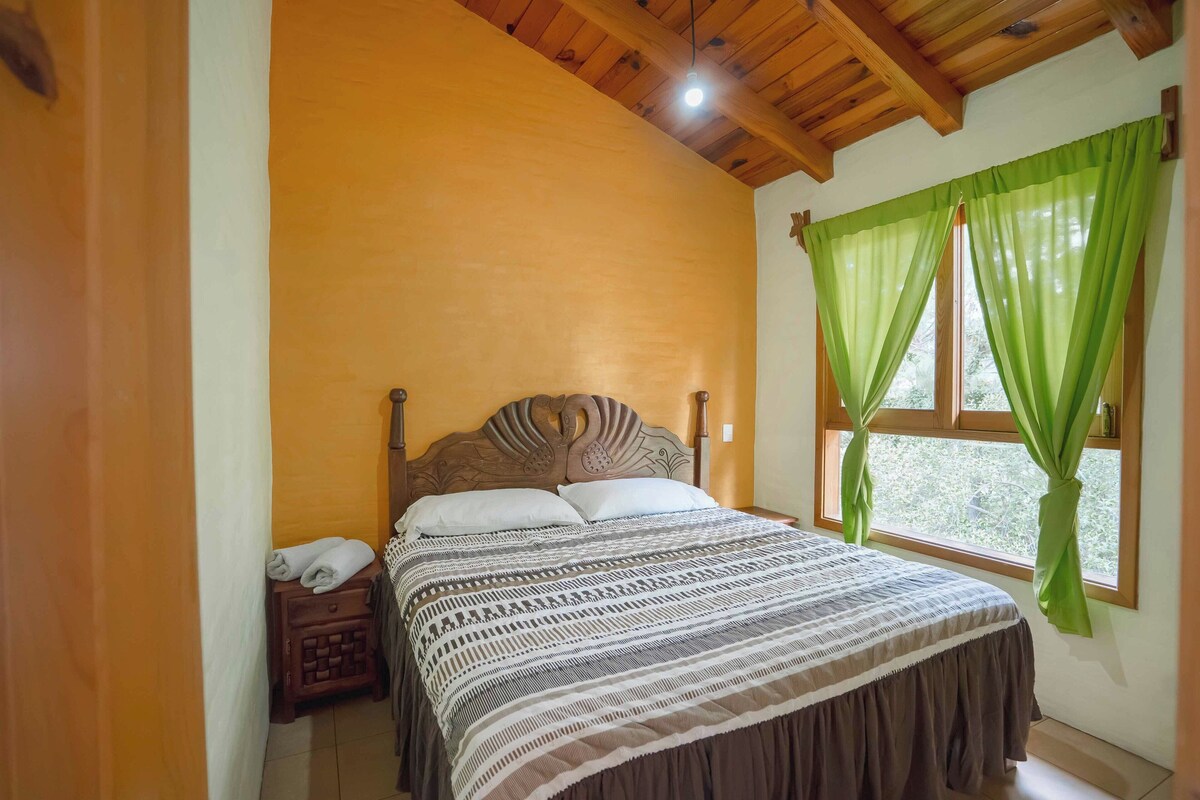 A bedroom with a wooden headboard, a bed with patterned bedding, a nightstand, and a window with green curtains.