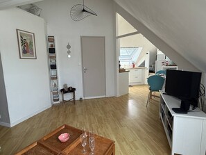Ein großzügiger Wohnbereich mit Holzboden, einem Esstisch mit Gläsern, einem Fernseher und einer kleinen Küche im Hintergrund.
