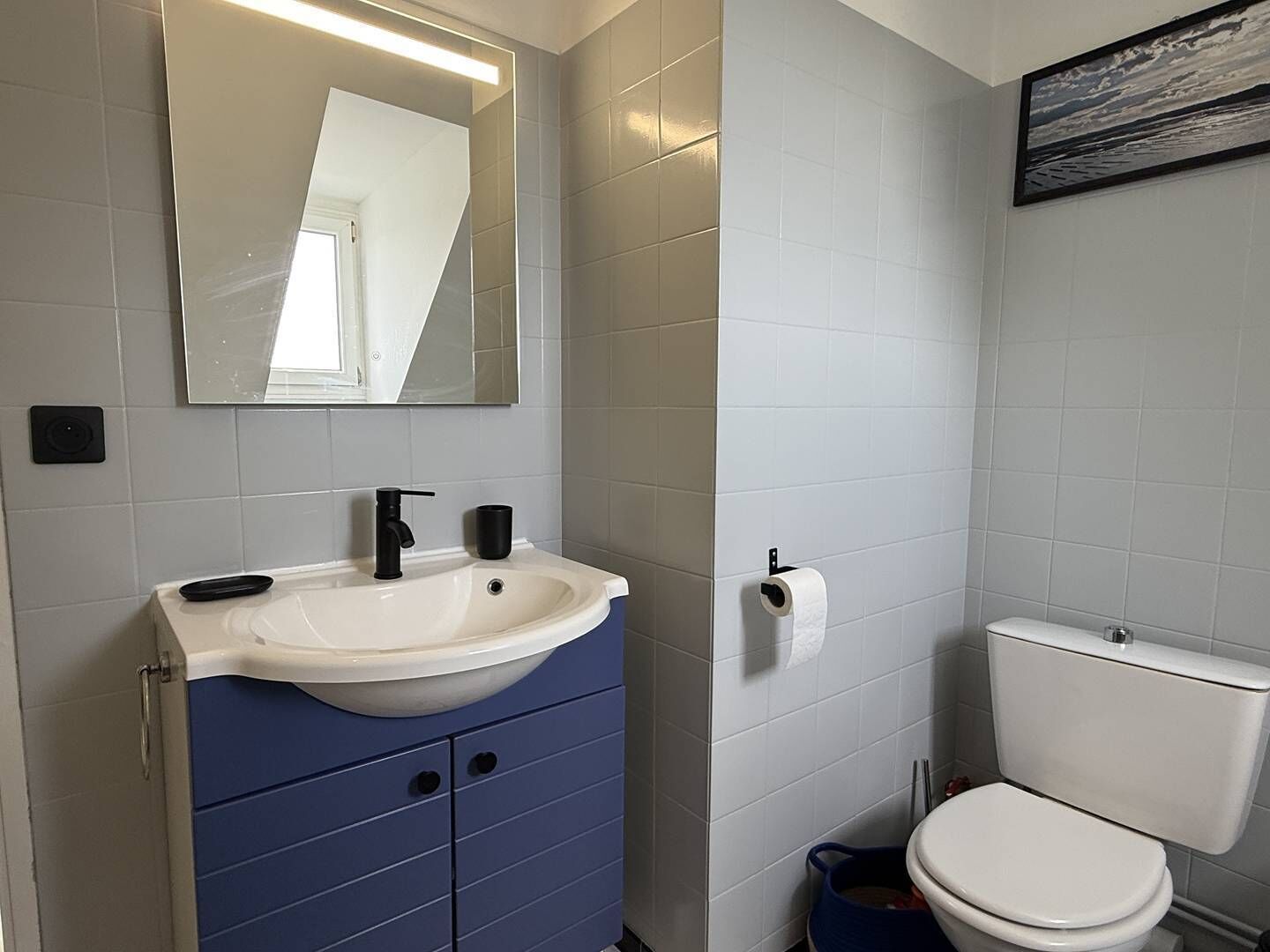 A bathroom with a white sink, blue cabinet, toilet, and a mirror.