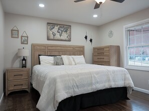 A bedroom with a wooden headboard, a bed with a white quilt, a nightstand with a lamp, a dresser, and a world map on the wall.