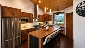 Een moderne keuken met houten kastjes, roestvrijstalen apparatuur en een centraal eiland met barkrukken.