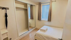 A bedroom with a bed, a closet, a window with curtains, and a mirror. - Fitzrovia 2 bedroom flat near the Britain museum (London)