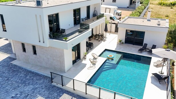 Et moderne hus med to etager, tagterrasse, swimmingpool og udendørs siddepladser.