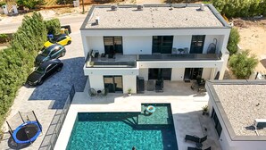 Et moderne hus med to etager, swimmingpool, udendørs møbler og en trampolin.