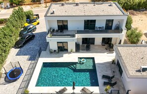 Ein modernes, zweistöckiges Haus mit Swimmingpool, Sitzgelegenheiten im Freien und einem Trampolin.