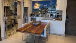 A modern kitchen with a wooden dining table, stainless steel appliances, and a view of a cityscape through a large window. - Garza Blanca Resort: Spacious 1,830 sq ft 2-bedroom suite for up to 6 guests. (Cancún)