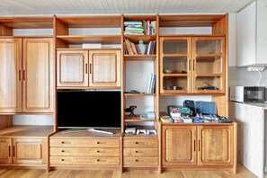 Un mueble de madera para entretenimiento con un televisor de pantalla plana, estanterías y consolas de videojuegos.