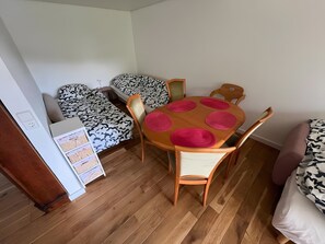 A small room with a wooden floor, a round table with pink placemats, two patterned beds, and a white cabinet.