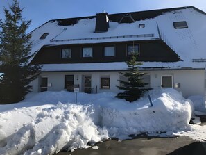 A building with a snow-covered roof, multiple windows, and a sign indicating parking availability.