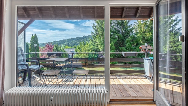 Ein Balkon mit Blick auf ein bewaldetes Gebiet, einer Holzterrasse und Gartenmöbel.