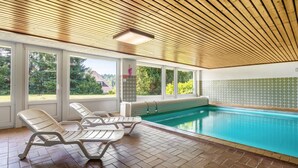 Ein Hallenbad mit klaren Fenstern, einer Holzbalkendecke und gefliesten Wänden.