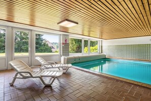Una piscina interior con ventanas amplias, techo de madera y paredes de azulejos.