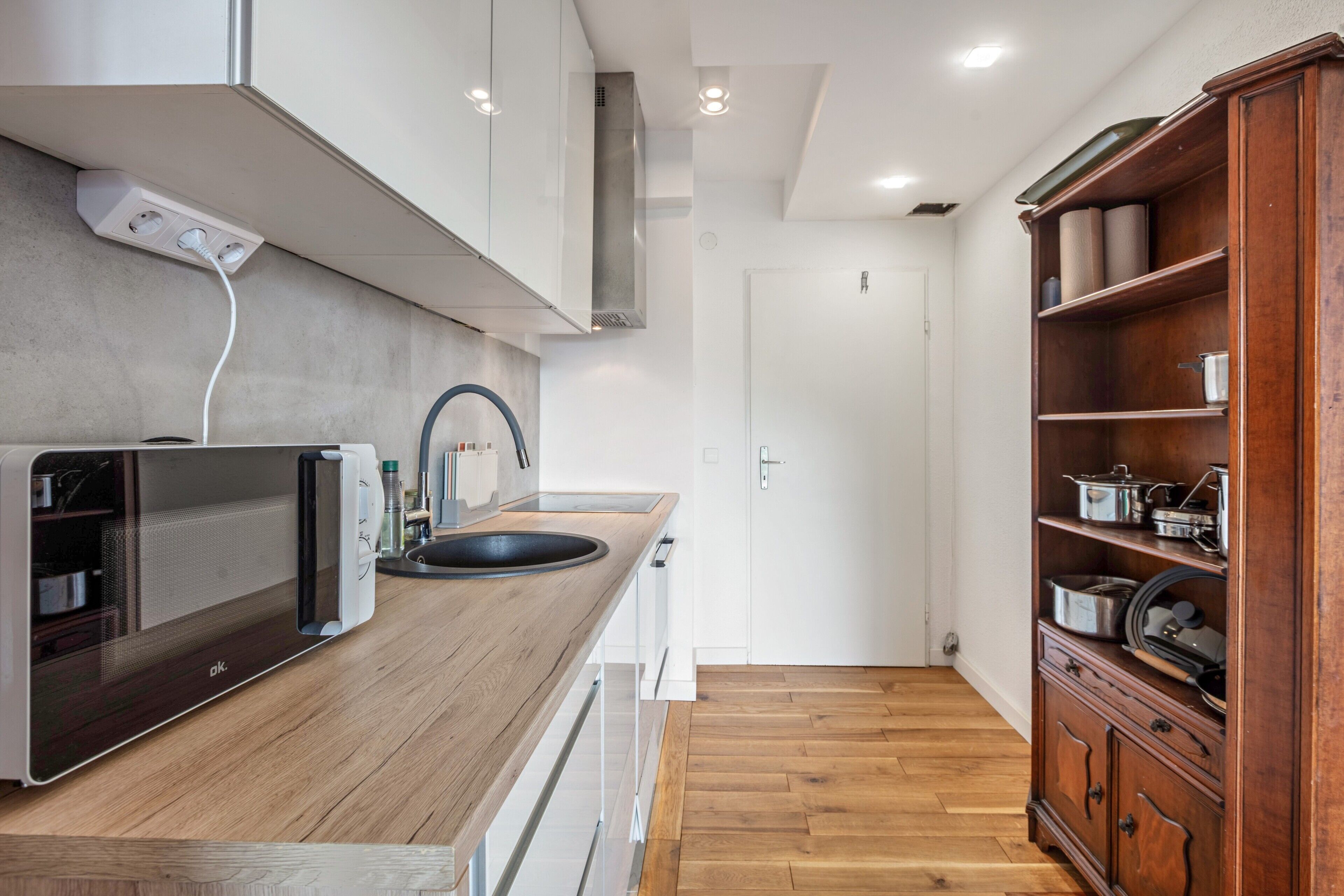 Una cocina moderna con microondas integrado, encimera de madera y un mueble de madera con utensilios de cocina.