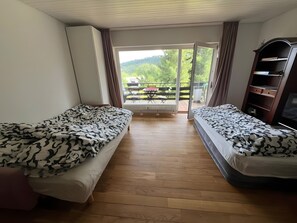 Ein Zimmer mit zwei Betten, Holzboden, einer Schiebetür zu einem Außenbereich mit Tisch und Stühlen sowie einem Fernseher auf einer Holzkommode.