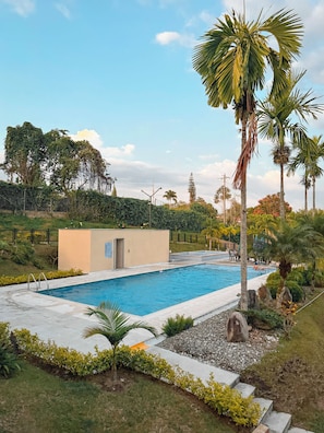 Una piscina amb un edifici petit, palmeres i una tanca.