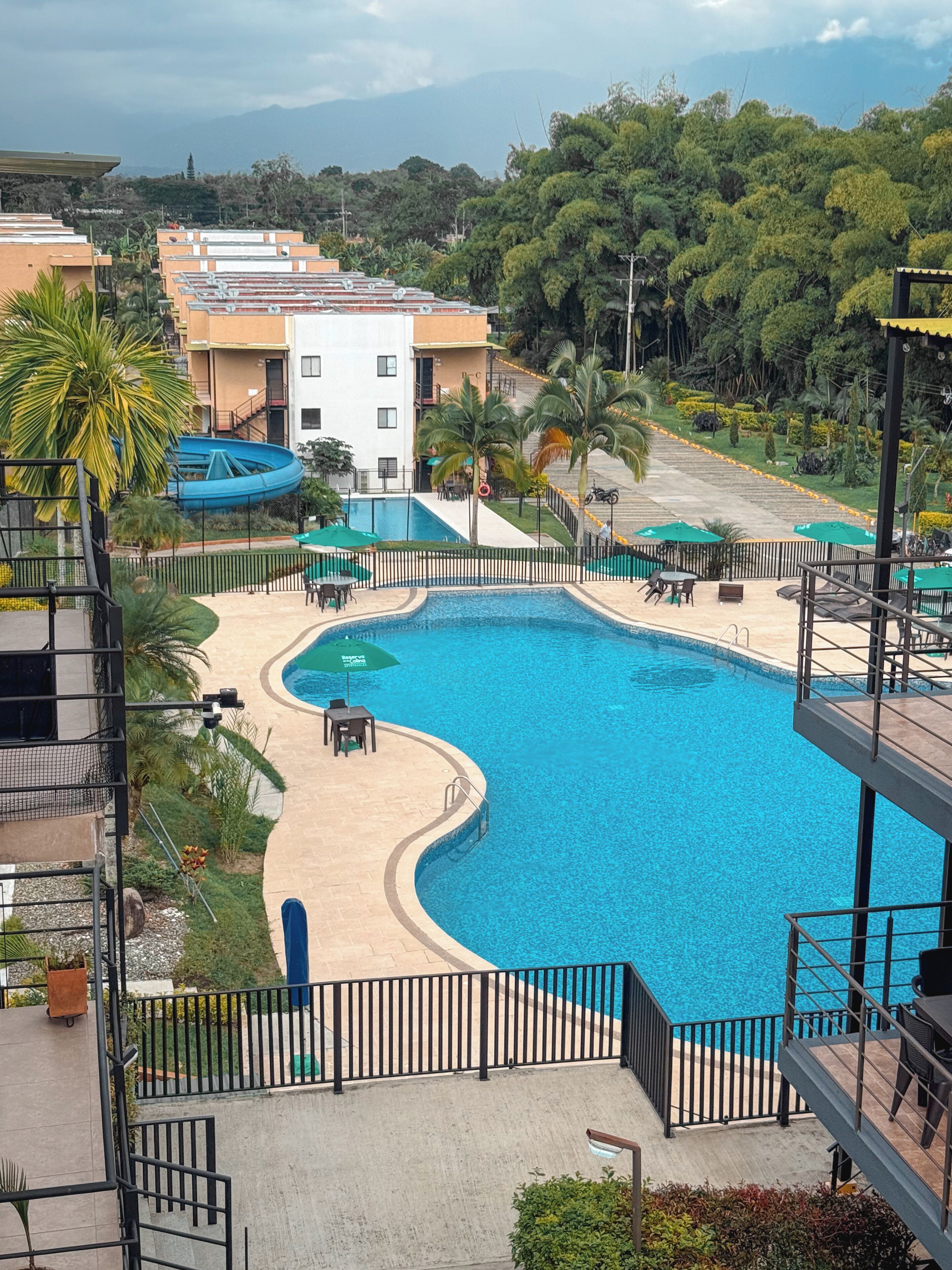 Une piscine à bord incurvé, entourée d’une clôture en métal noir, et un bâtiment avec des balcons en arrière-plan.