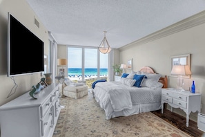 Ein Schlafzimmer mit Bett, Kommode, Fernseher und Blick auf den Strand.