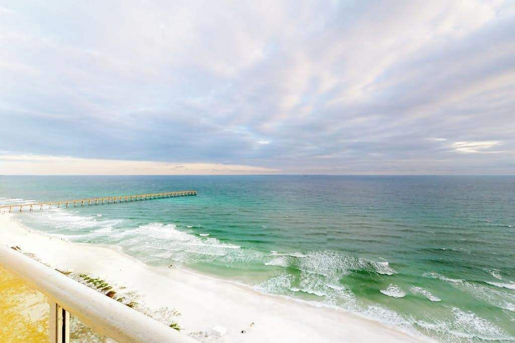 A beach with a pier extending into the ocean, a sandy shore, and a cloudy sky.